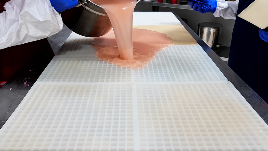 Gummy Moldsチームが大型商業用シリコンモールドにグミ液を流し込み、余分をスクレープする前の様子